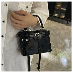 Detail of a black patent leather box bag with vintage stitching and gold metal hardware