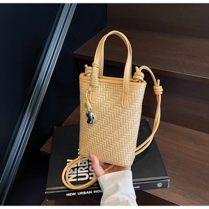 Détail du mini sac seau tressé jaune avec breloque cœur argentée et bandoulière