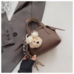 Détail d'un sac à main marron en cuir grainé avec un pendentif ours sur une veste grise