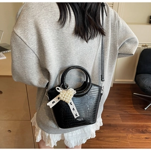 Detail of black crocodile texture bag with pearl heart charm worn by a model