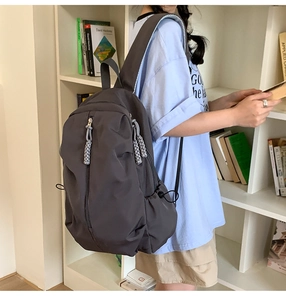 Detail of dark grey nylon backpack featuring woven zipper pulls and side drawstring pockets
