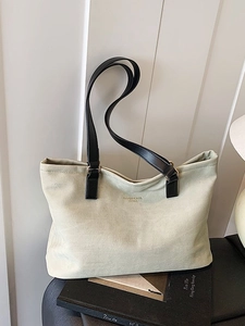 Minimalist canvas tote bag with black leather straps and metal rings in a top-down view