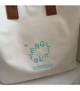 Detailed shot of cream canvas tote bag with mint green embroidery and brown leather handle