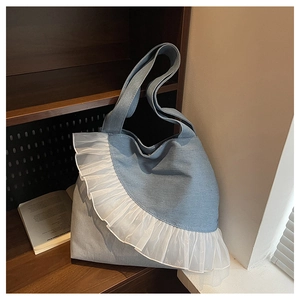 Detailed shot of large denim tote bag featuring white lace ruffle trim on wooden shelf