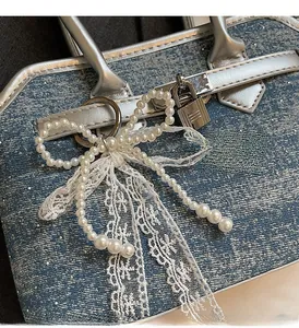 Gros plan du pendentif nœud en perles avec rubans en dentelle sur sac bleu