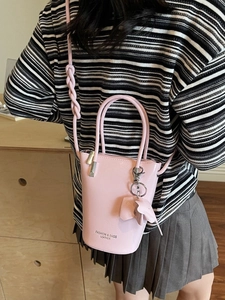 Pink bucket bag with elephant charm and woven strap detail shown from a side view