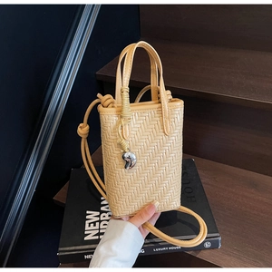 Détail du sac seau tressé beige avec pendentif argenté et bandoulière à nœud