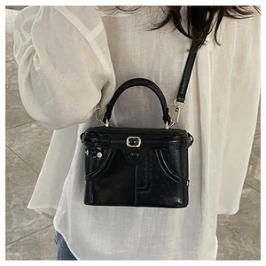 Detail of a retro black box bag with shiny finish and gold metal hardware strap loops