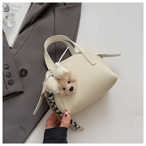 Détail d'un sac à main en cuir grainé crème avec charme d'ours en peluche et foulard