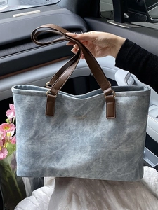 Blue denim tote bag with brown leather handles and fashion printed text on the front