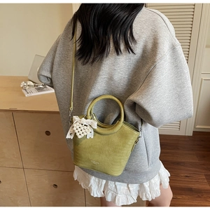 Detail of green crocodile embossed handbag with pearl heart charm and lace bow decor