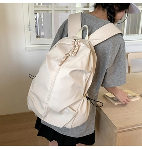 Detail of beige nylon backpack with braided zipper pulls and elastic side pockets