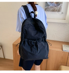 Detail of black nylon backpack featuring drawstring front pocket and textured matte fabric