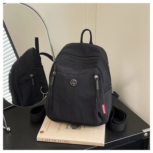 Détail d'un sac à dos en nylon noir avec logo métallique posé sur un magazine