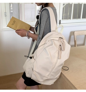 Detail view of the beige nylon backpack featuring side drawstring pockets and braided zipper pulls