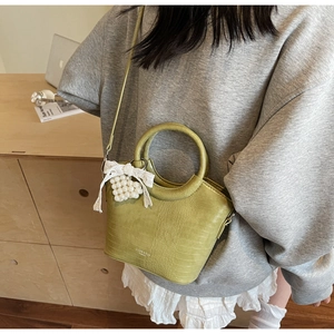 Detail of green faux crocodile skin handbag with pearl lace pendant and round handle