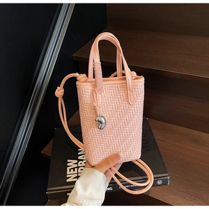 Détail du mini sac seau tissé rose clair avec pendentif argenté sur fond en bois