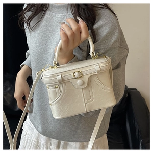 Detail of a structured cream leather box bag with a golden buckle and round top handle