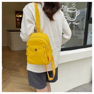 Détail d'un mini sac à dos en nylon jaune avec deux fermetures éclair et étiquette tissée