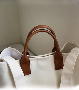 Detail of durable canvas tote with brown leather handles and reinforced stitching
