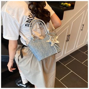 Detail view of denim bucket bag with silver handle and star tassel charm on a model