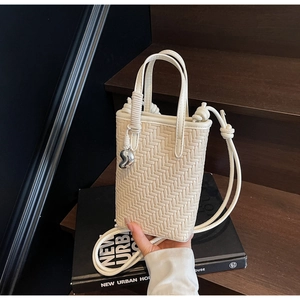 Détail d'un sac seau tressé crème avec poignée en corde torsadée et pendentif en métal