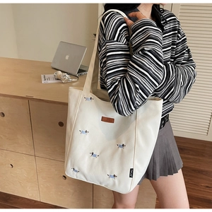 Detail of embroidered dachshund patterns on a beige canvas tote bag over the shoulder