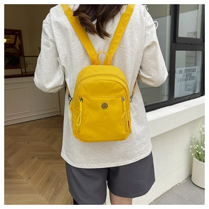Nahaufnahme des hellgelben Mini-Rucksacks mit rundem Logo und zwei Front-Reißverschlussfächern