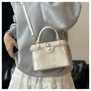 Detail of a vintage-style cream leather box bag with decorative stitching and gold hardware