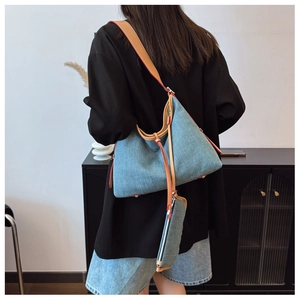 Detail of blue denim tote bag with brown leather trim worn by a model in a modern room
