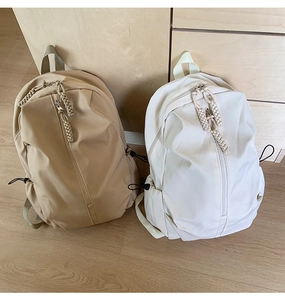Detail of khaki and beige nylon backpacks featuring vertical zippers and woven pullers