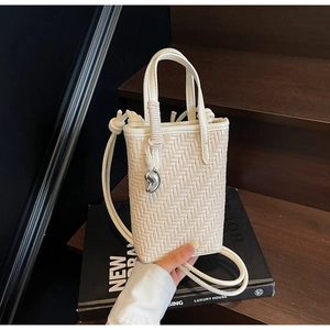Détail du sac seau tressé crème avec breloque cœur argentée sur escalier