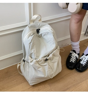 Detail view of cream nylon backpack featuring black drawstring side pockets and top handle