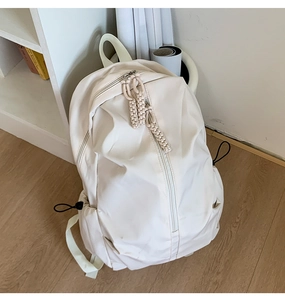 Minimalist beige backpack on light wood floor with vertical zipper and drawstring side pockets