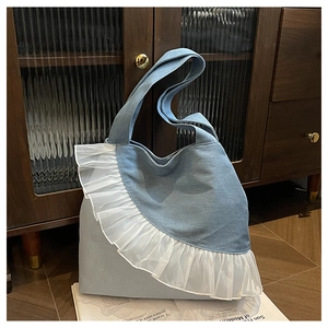 Detail of blue denim tote bag featuring white organza ruffle trim and wide shoulder strap