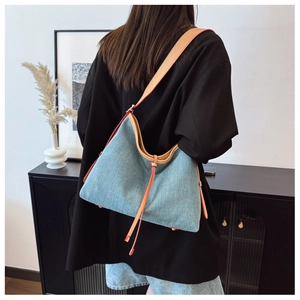 Detail of light blue denim hobo bag featuring brown leather strap and red painted edges