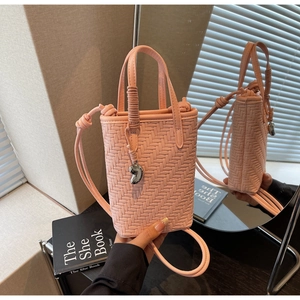 Détail d'un sac seau rose tressé avec breloque métallique et bandoulière à nœud