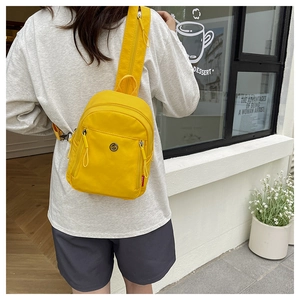Détail du sac bandoulière en nylon jaune avec plusieurs zips et logo métallique rond
