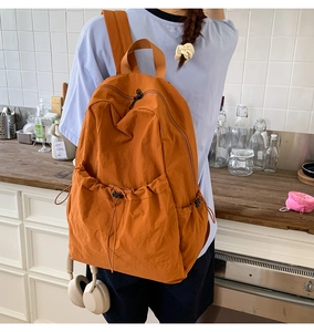 Detail of a bright orange nylon backpack showing the front drawstring pocket and side pouch