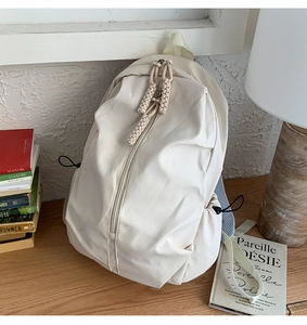 Detail of off-white nylon backpack featuring woven zipper pulls and side drawstring pockets