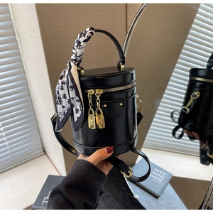 Detail of black cylindrical crossbody bag with gold padlock and silk scarf handle accent