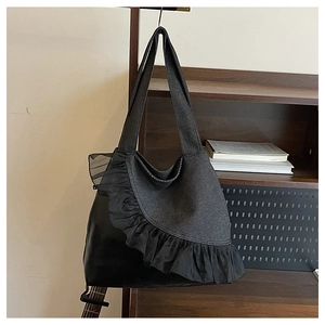 Detail of black tote bag featuring textured fabric panels and elegant lace ruffle trim
