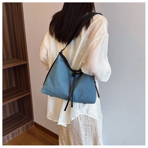 Blue denim tote bag detail featuring black leather straps and stylish tassel drawstring