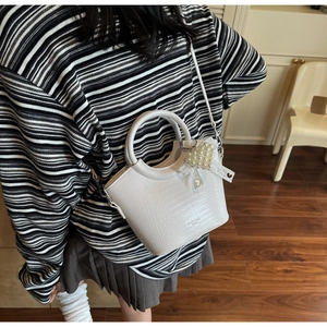 Detail of white crocodile pattern bucket bag with pearl heart charm and lace bow
