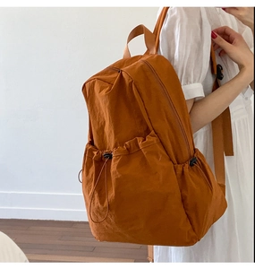 Detailed view of caramel nylon backpack featuring drawstring side pockets and top handle