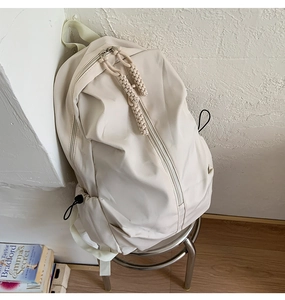 Detail of off-white nylon backpack featuring woven rope zippers and side drawstring pockets