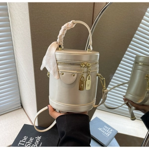 Detail of cream cylindrical bucket bag with gold hardware and satin wrapped handle
