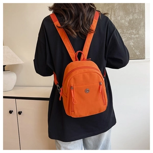 Detail eines leuchtend orangefarbenen Nylon-Minirucksacks mit Metalllogo und Doppelreißverschluss