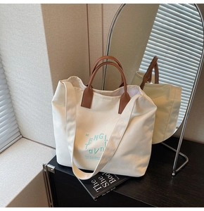 Détail du sac cabas en toile blanche avec broderie bleue et poignée en cuir marron