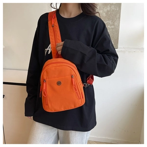 Détail du sac bandoulière en nylon orange vif avec logo métallique rond et fermetures éclair